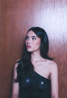 a woman standing in front of a wooden wall with her hand on her hip and looking off to the side