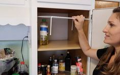 a woman is opening the door to a cupboard filled with bottles and condiments