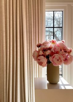 a vase filled with pink flowers sitting on top of a table next to a window