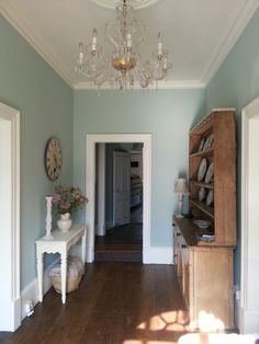 an empty room with a chandelier and table in the corner, next to a doorway