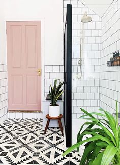 a bathroom with black and white tiles, pink door and potted plant on the floor