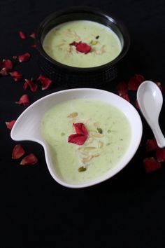 two bowls filled with soup next to spoons and rose petals on a black surface