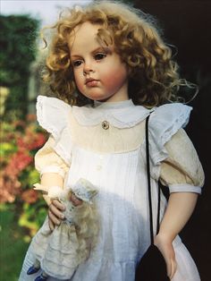 a doll with curly hair holding a stuffed animal in her hands and looking at the camera