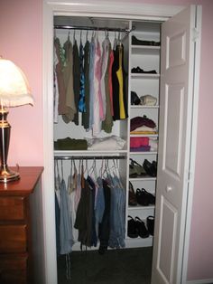 an open closet with clothes and shoes hanging on the shelves, next to a lamp