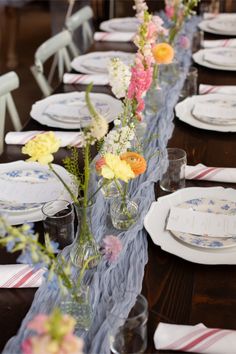 a long table is set with plates and flowers in glass vases on the tables