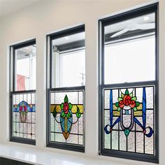 three stained glass windows with flowers on them in a white walled room, each window has four different designs