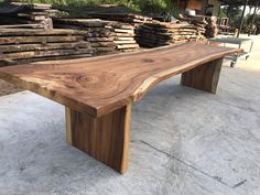 a large wooden bench sitting on top of a cement floor next to stacks of logs