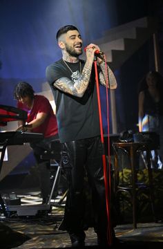 a man with tattoos on his arm holding a microphone and singing in front of other people