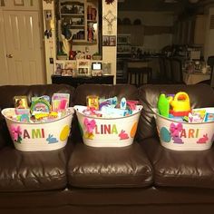 three buckets filled with toys sitting on top of a brown couch in a living room