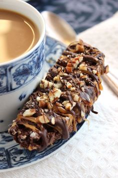 a cup of coffee next to a piece of chocolate covered pastry on a blue and white plate