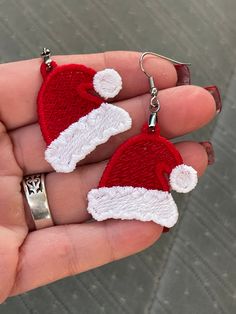 two red and white knitted santa hats on small silver earring hooks in the palm of someone's hand