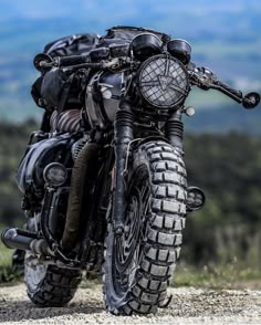 a black motorcycle parked on top of a dirt road next to a lush green hillside