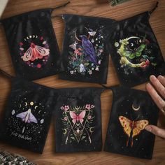 four bags with embroidered designs on them are sitting on a table next to a person's hand