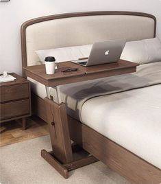 a laptop computer sitting on top of a wooden desk next to a bed with white sheets