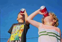 two young boys standing next to each other holding cans of soda in front of their eyes