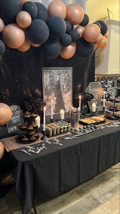 a table topped with lots of desserts next to a black and gold balloon wall