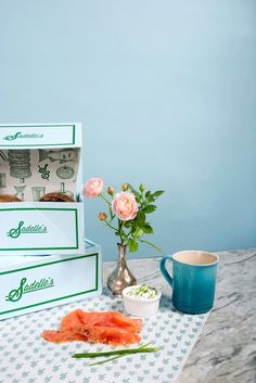 two boxes of sushi and some flowers on a table next to a coffee cup