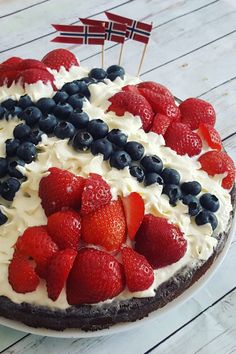 a cake decorated with strawberries and blueberries on a white wooden table next to a flag