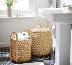 two wicker baskets sitting on the floor next to a white sink and window in a bathroom