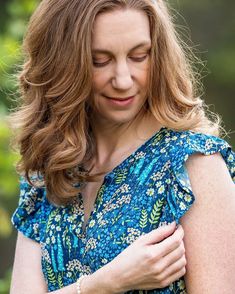 a woman in a blue floral dress holding her arm around her chest and looking down