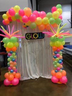 an arch made out of balloons with the word glow written on it and streamers