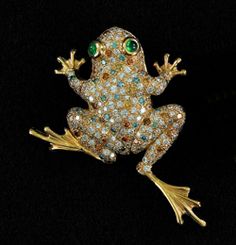 a frog brooch with green eyes sitting on a black surface in front of a black background