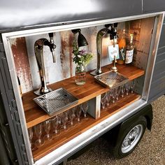 an outdoor bar with wine glasses and bottles on the outside wall, in front of a trailer