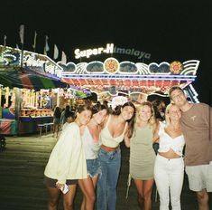 a group of young people standing in front of a carnival ride at night with their arms around each other