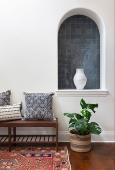 a white vase sitting on top of a wooden bench next to a potted plant