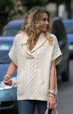 a woman walking down the street with her hand in her pocket and wearing a white sweater