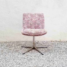 a pink chair sitting on top of a gravel covered floor next to a white wall