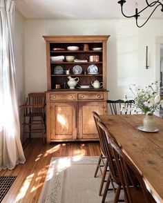 a dining room table with chairs and a hutch in the corner that has plates on it