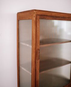 a wooden cabinet with glass doors on the front and bottom sides, against a white wall