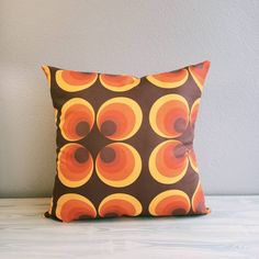 an orange and brown pillow sitting on top of a white table next to a gray wall