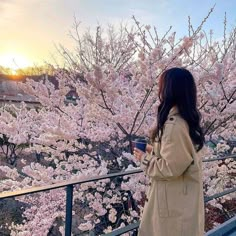 a woman standing in front of a tree with pink flowers and holding a coffee cup