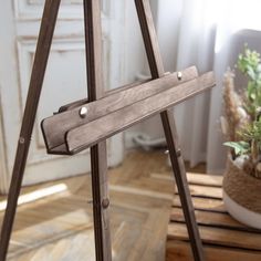 a wooden easel sitting on top of a hard wood floor next to a potted plant