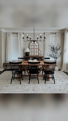 a dinning room table and chairs in front of a window with white drapes