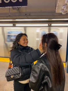 two women standing next to each other in front of a subway train at a station