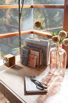 a wooden table topped with books and vases filled with flowers next to a window