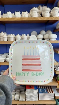 a person holding up a plate with candles on it in front of shelves full of plates