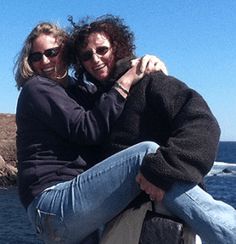 two women sitting on the back of a boat in front of an ocean and rocks