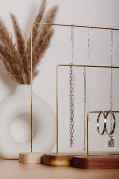 a white vase sitting on top of a wooden table next to earrings and a plant