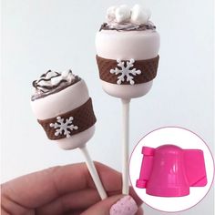 two marshmallow lollipops with chocolate frosting and white decorations on them