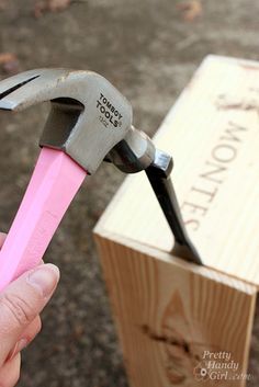 a person holding a pink handled wrench in front of a wooden box