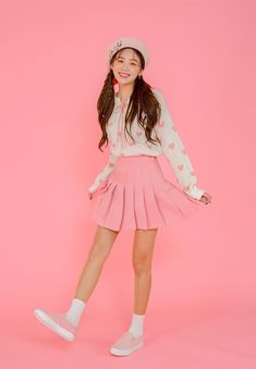 a girl in pink skirt and white shirt posing for the camera with her hands on her hips