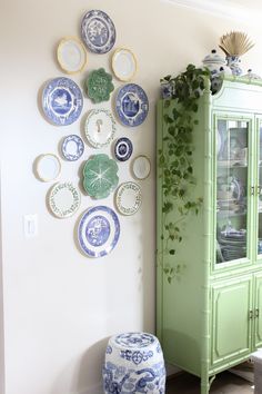 a green china cabinet sitting next to a wall with plates hanging on it's side