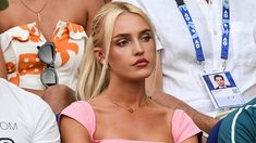 a woman sitting in the stands at a tennis match wearing a pink top and sunglasses