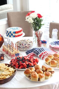 a table topped with lots of food next to a vase filled with red white and blue flowers