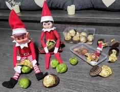 two elfs are sitting on the floor with some candy and nuts in front of them