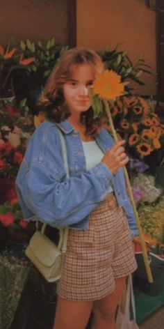 a young woman holding a yellow flower in her right hand and looking at the camera